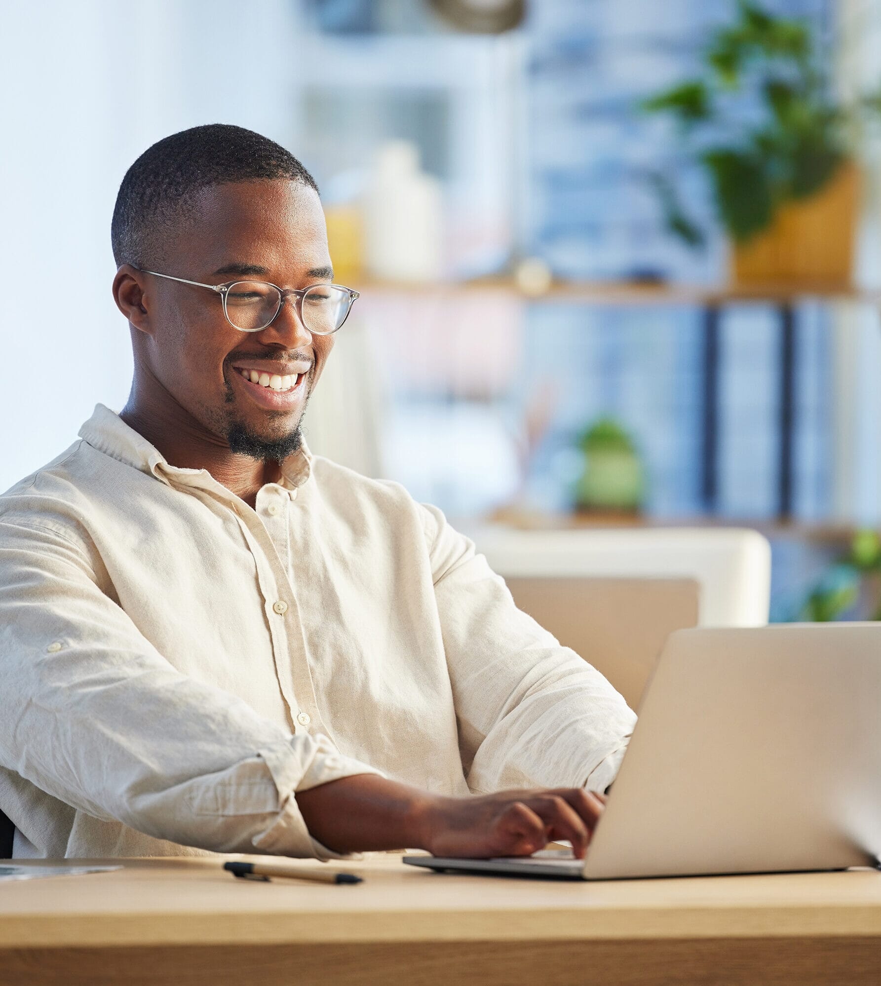 A black business payroll services employee on a laptop typing. He's wearing a smart white shirt, glass and has a a goatee.