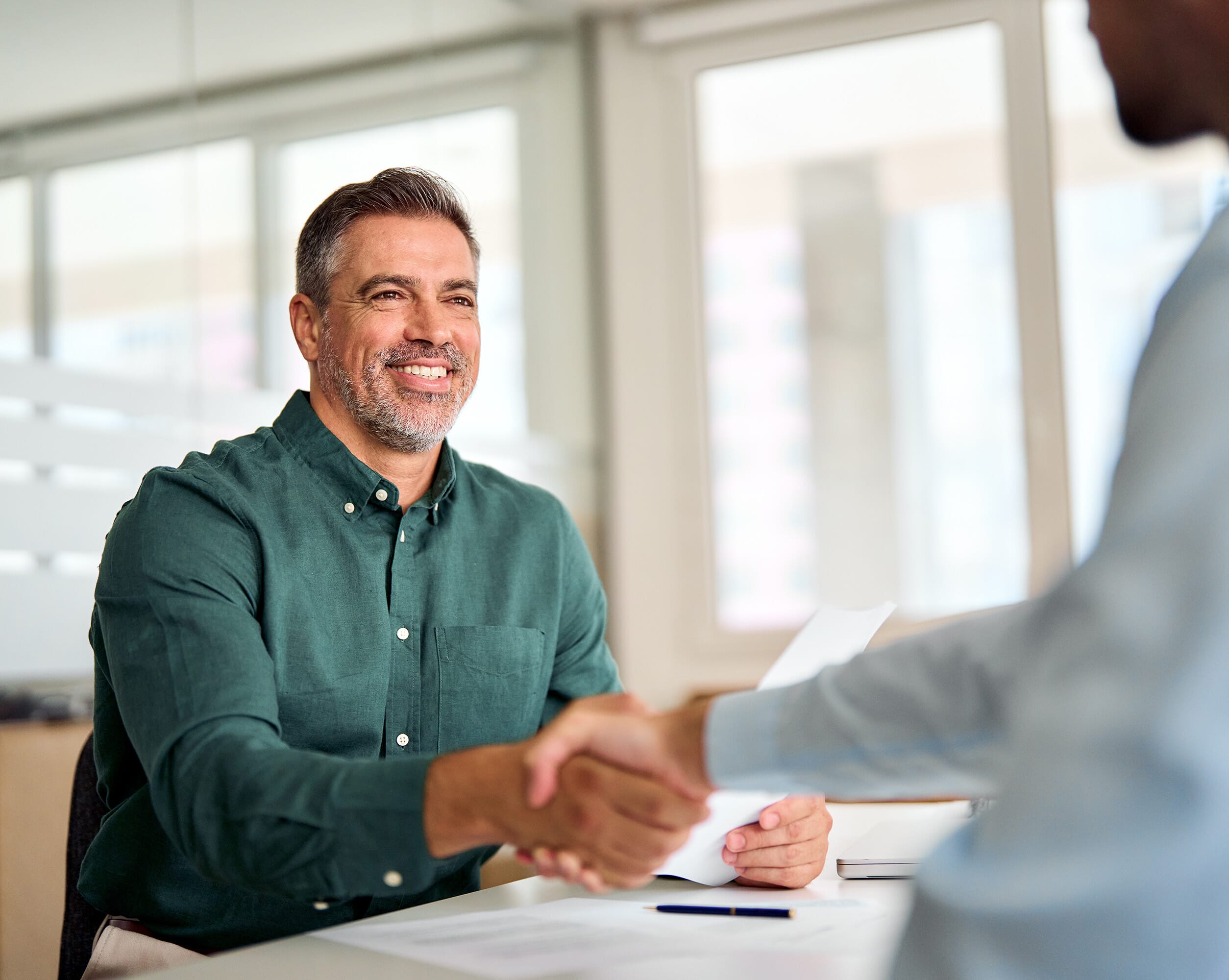 A white male employee in a green shirt shaking hands with a client around HR consultancy