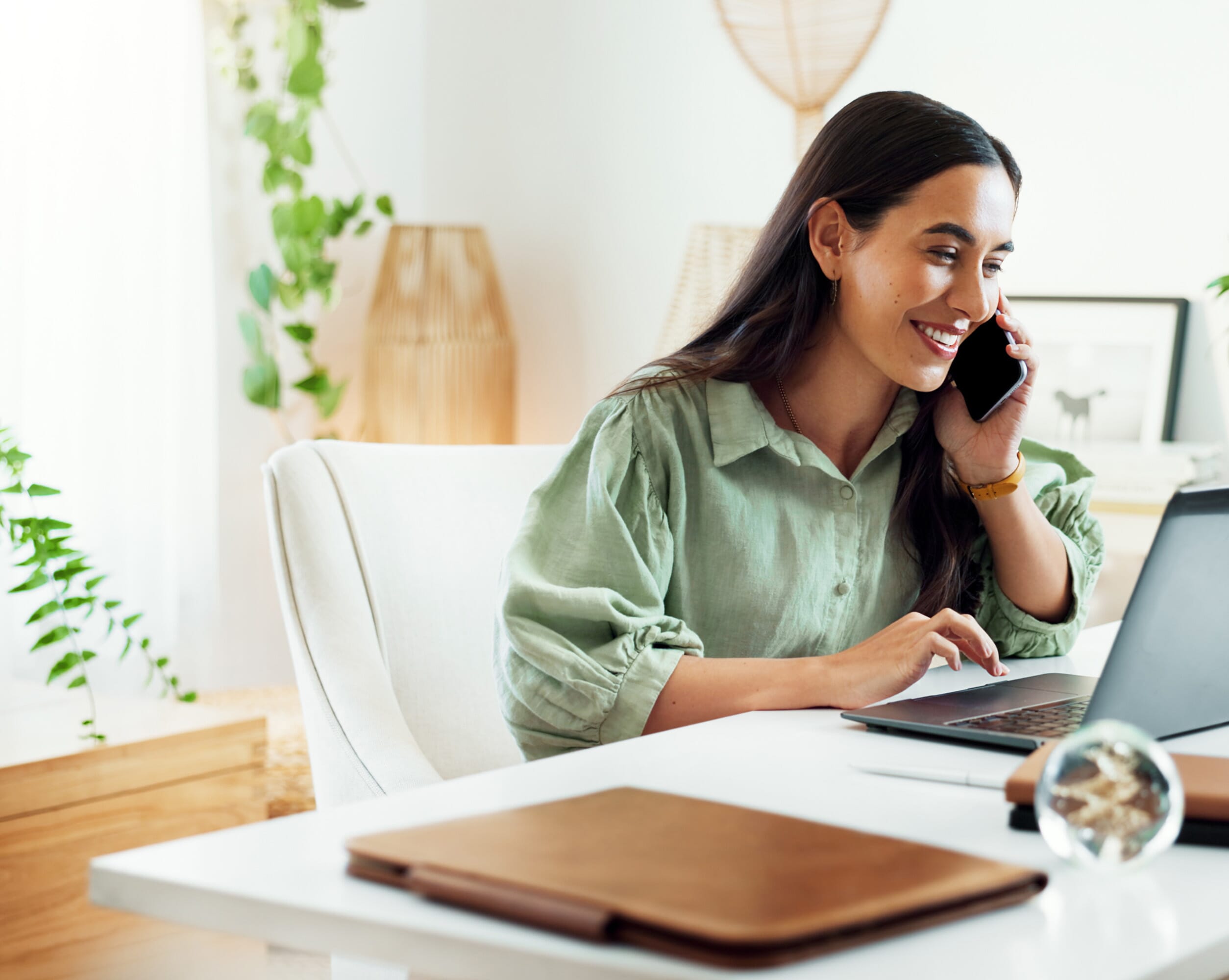 A happy lady in a green shirt talking on a mobile phone sat at a desk in a bright white room. Hire global talent seamlessly with our Employer of Record (EOR) service. We handle compliance, payroll, and employment contracts in over 160 countries, simplifying expansion.