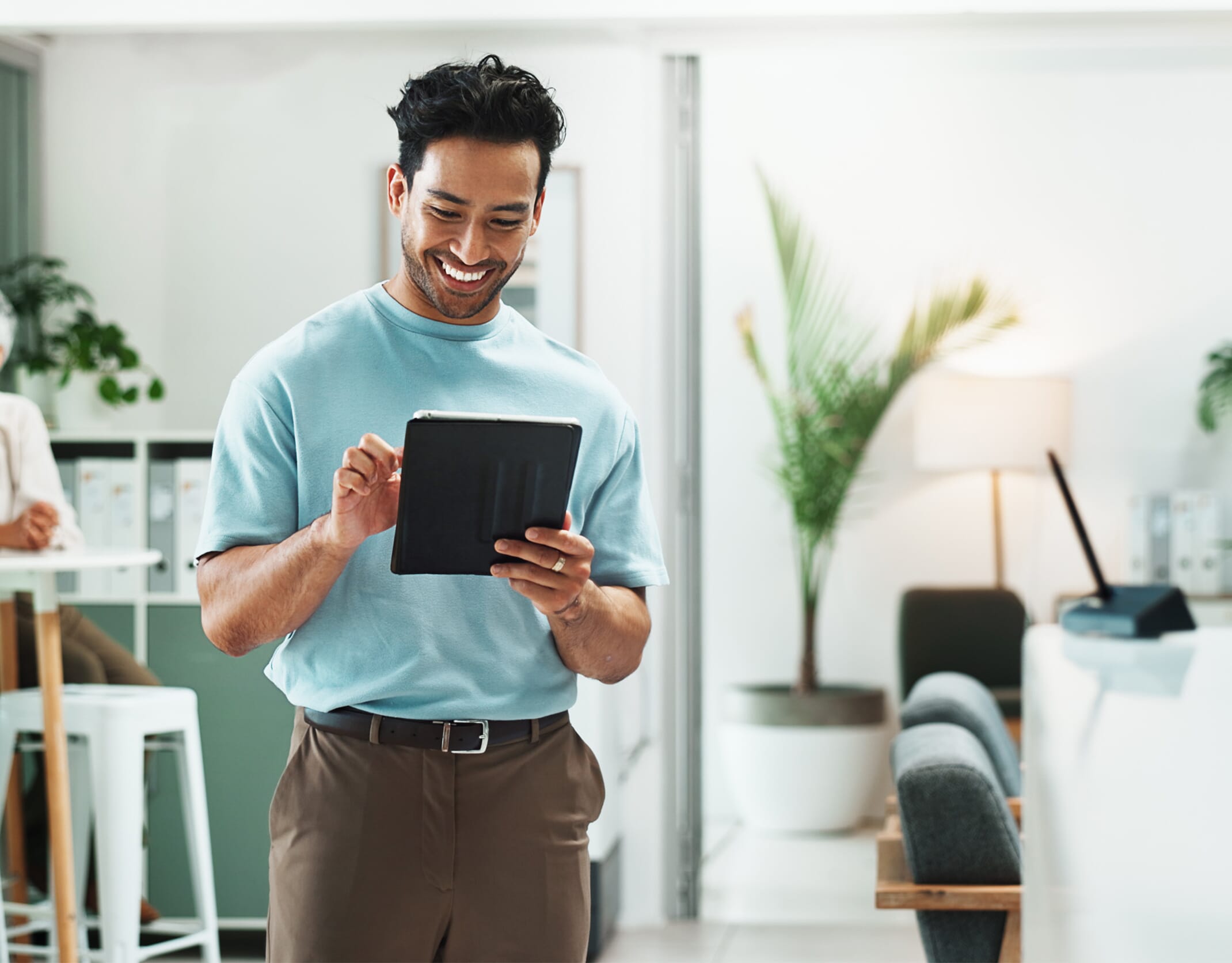 Smartly dressed man stood smiling on an ipad in a light office background. Employee Benefits Consultancy