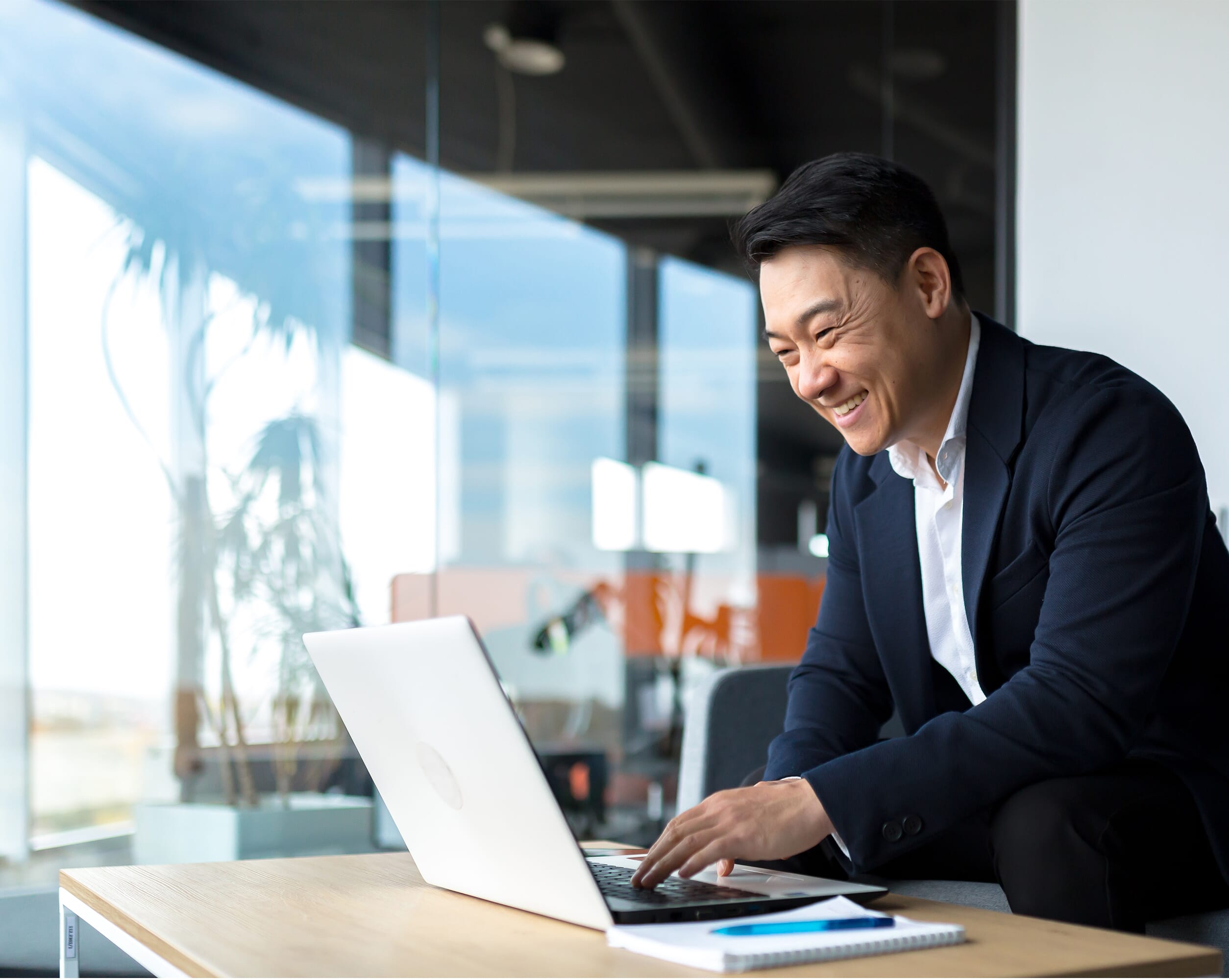 An smartly dressed asian male in a light office working on a laptop. Global outsourcing services